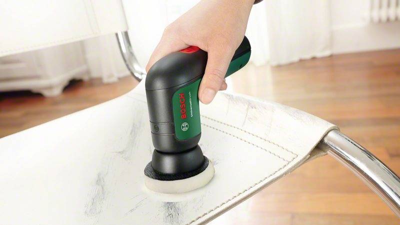 Ruka drží elektrický leštič, ktorý sa vedie po bielej ploche stoličky za účelom čistenia alebo leštenia.