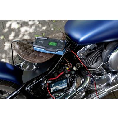 Motocykel s pripojenou batériou a nabíjačkou položenou na sedadle. Displej zobrazuje stav nabíjania.