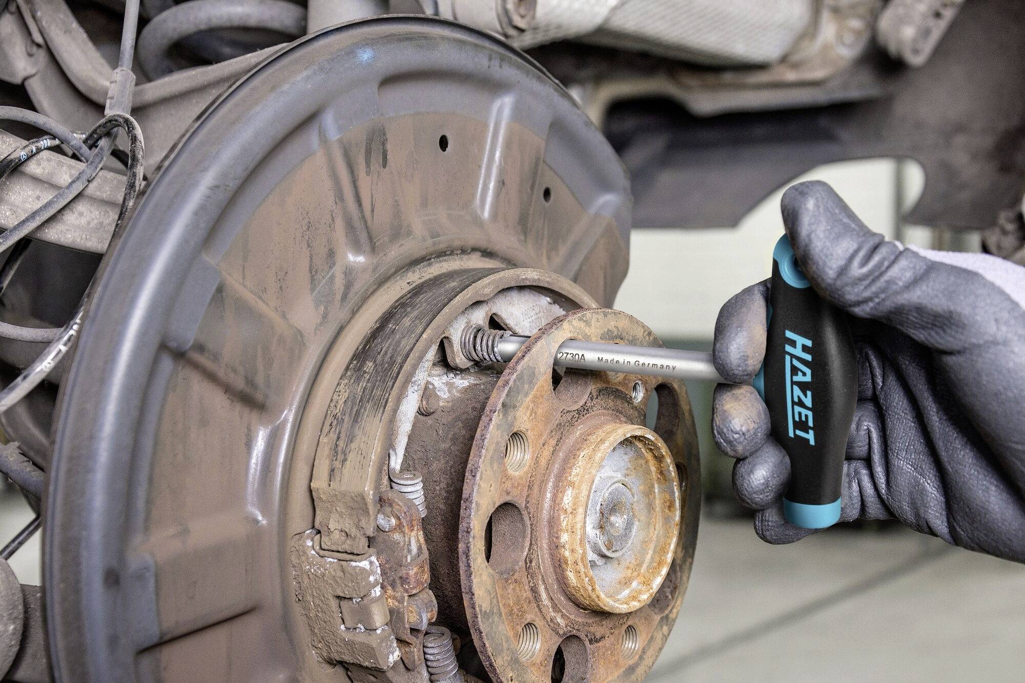 Mechanik uťahuje skrutku na brzdovom systéme automobilu pomocou nástroja značky Hazet. Záber je zameraný na brzdový kotúč.