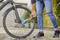 Osoba čistí prednú pneumatiku bicykla kefou a prúdom vody na dlažobnej príjazdovej ceste.