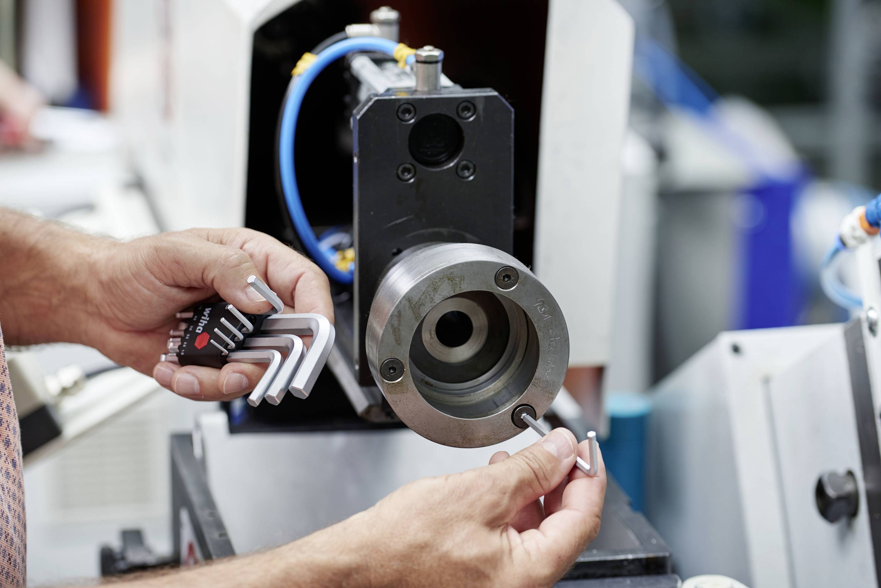 Osoba nastavuje CNC stroj pomocou inbusových kľúčov. V pozadí sú viditeľné strojové diely a káble.