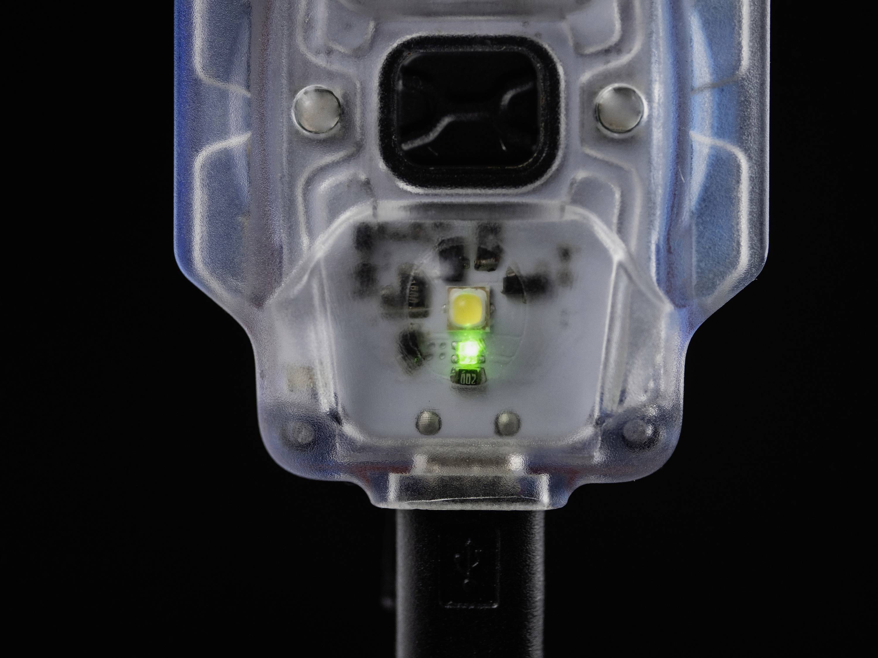 Detailný záber priehľadného elektronického zariadenia so zelenou LED diódou v strede na čiernom pozadí.