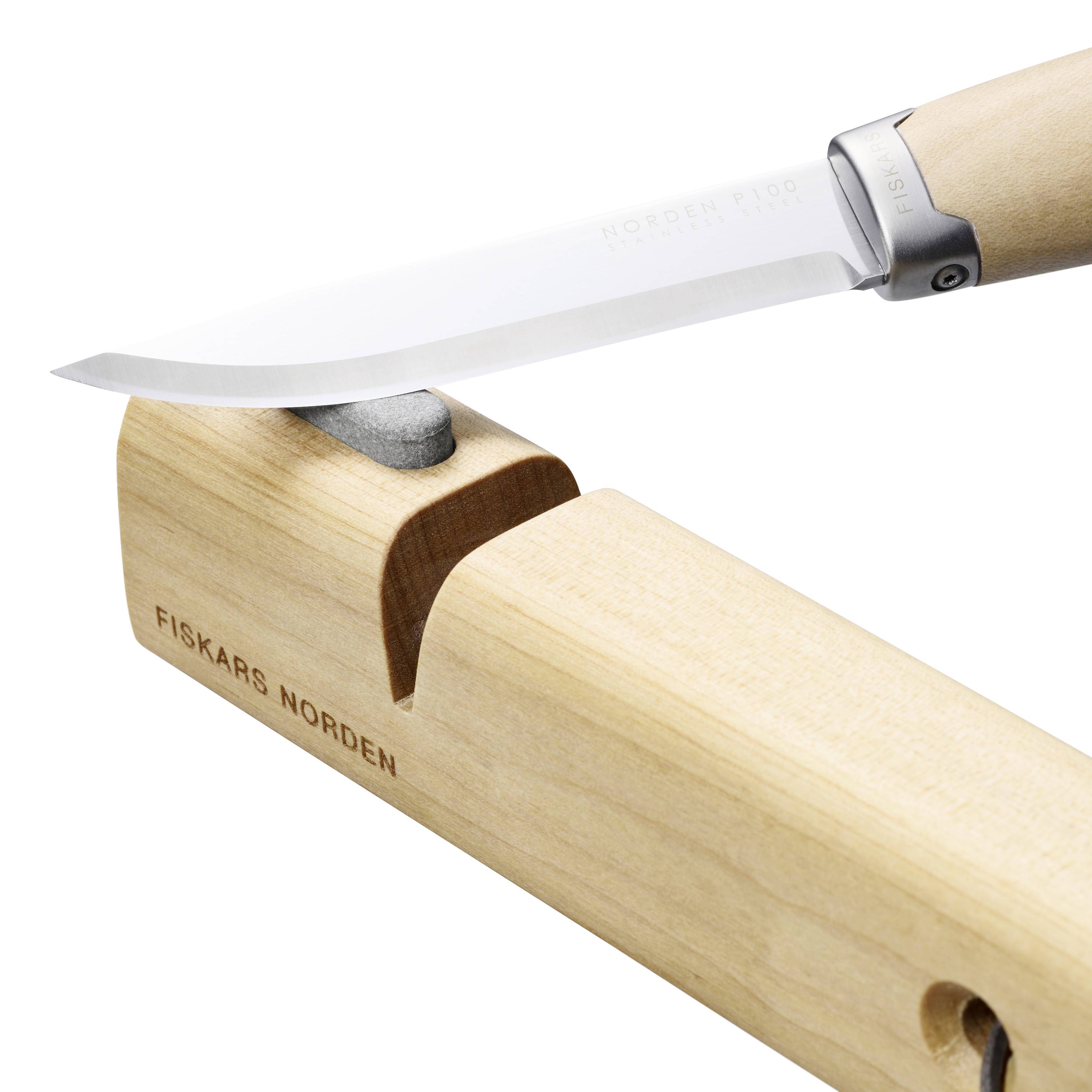 Nôž sa brúsi na brúsnom kameni. Drevená rukoväť kameňa má nápis 'Fiskars Norden'.