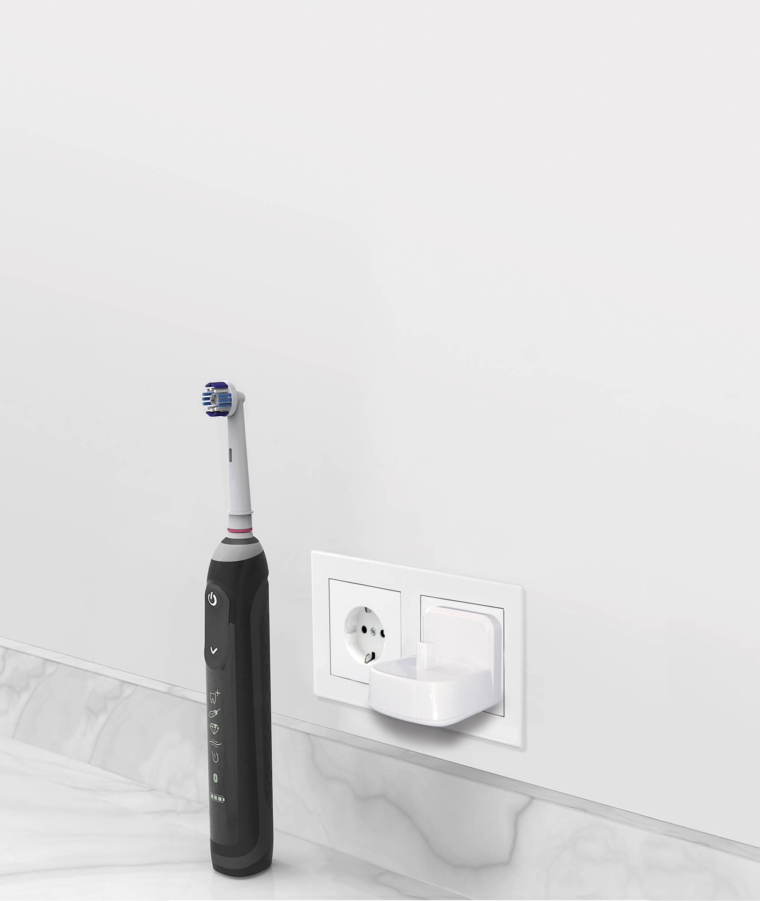 Elektrická zubná kefka v čiernej farbe stojí na bielom kúpeľňovom umývadle vedľa elektrickej zásuvky s nabíjačkou.