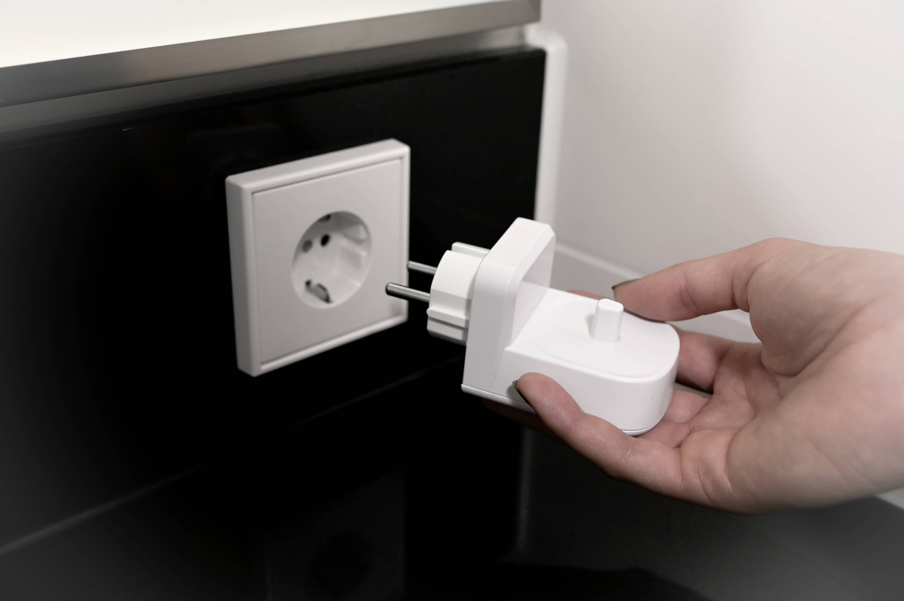 Ruka zasúva bielu zástrčku do elektrickej zásuvky na stene.