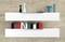 Dve biele police na stene. Na hornej polici stoja vázy a miska. Spodná polica je zaplnená farebnými chrbtami kníh.