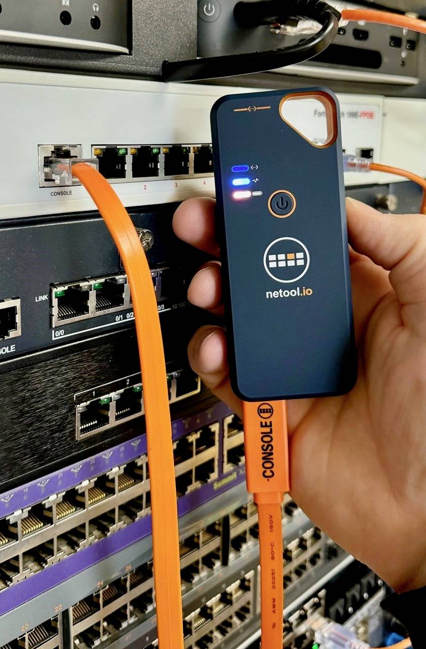 Ruka drží nástroj na analýzu siete, prepojený oranžovým káblom so serverom v racku. LED kontrolky na zariadení indikujú jeho stav.