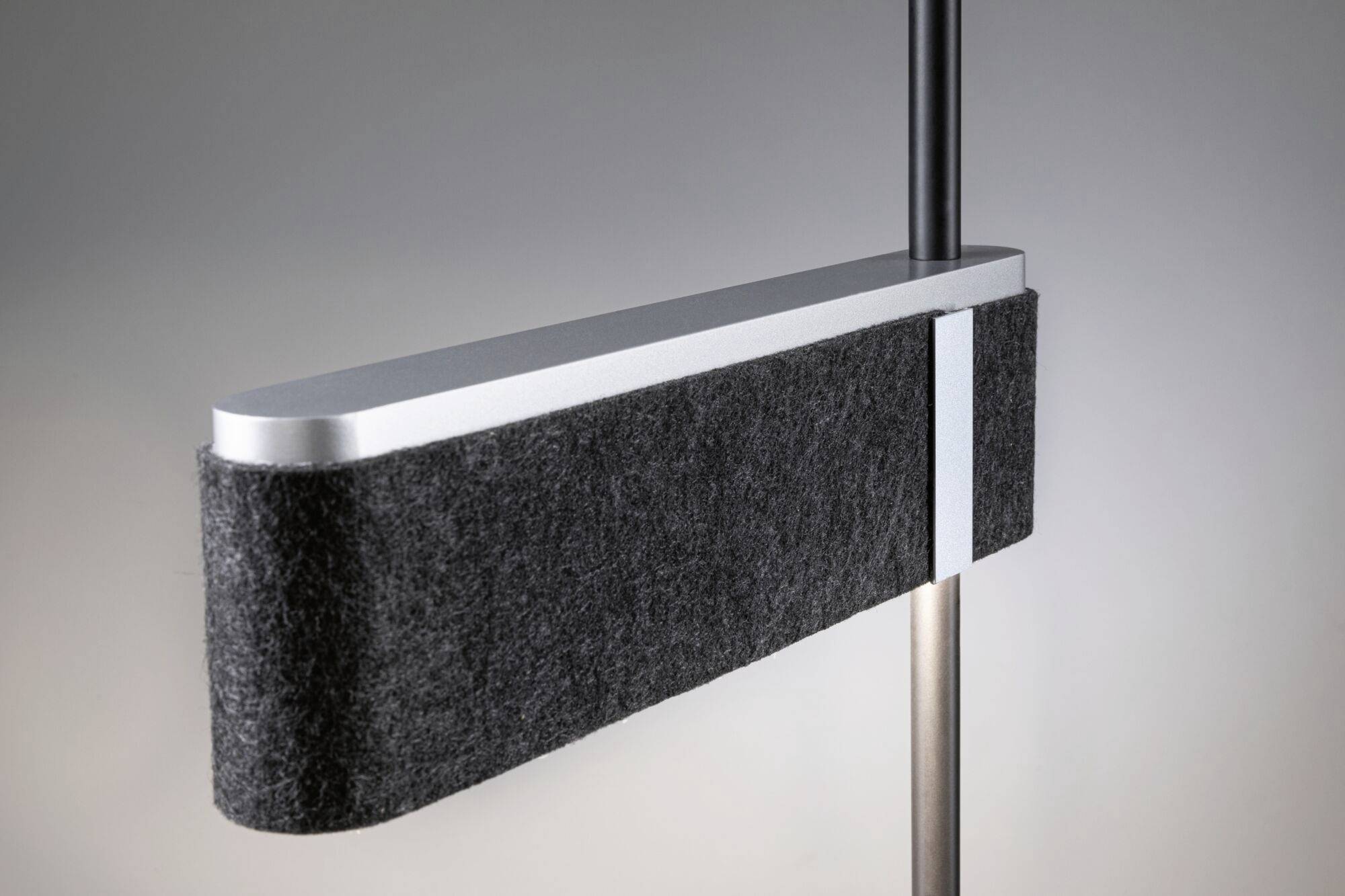 Moderná, obdĺžniková lampa s sivým plsteným poťahom a kovovým povrchom na štíhlom čiernom podstavci.