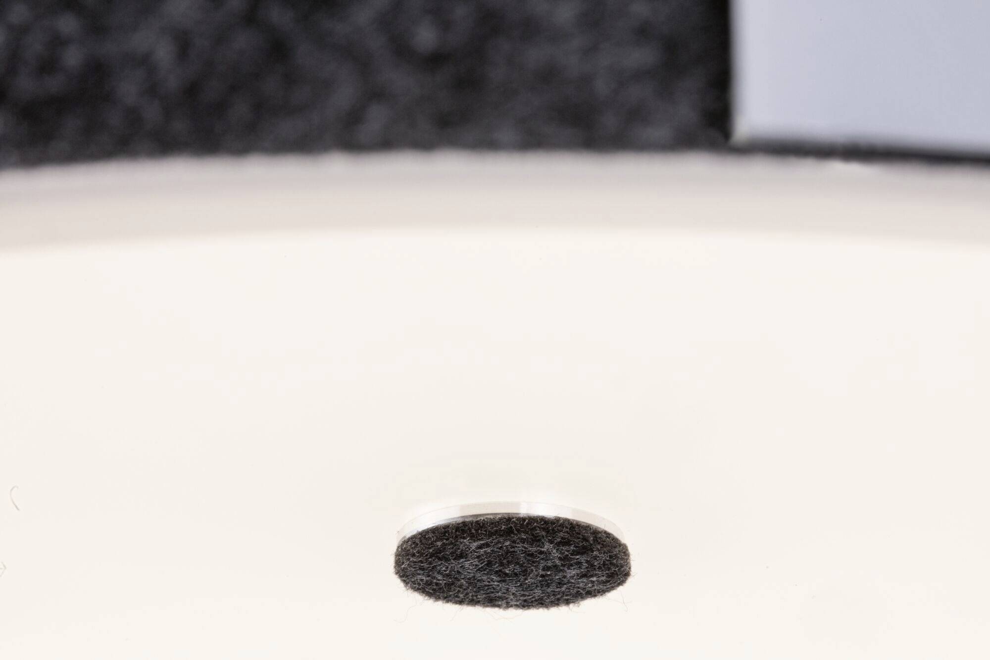 Guľatý, tmavý plstený kĺzač na hladkom, bielom povrchu. Vľavo hore je viditeľné nejasné, tmavé pozadie.