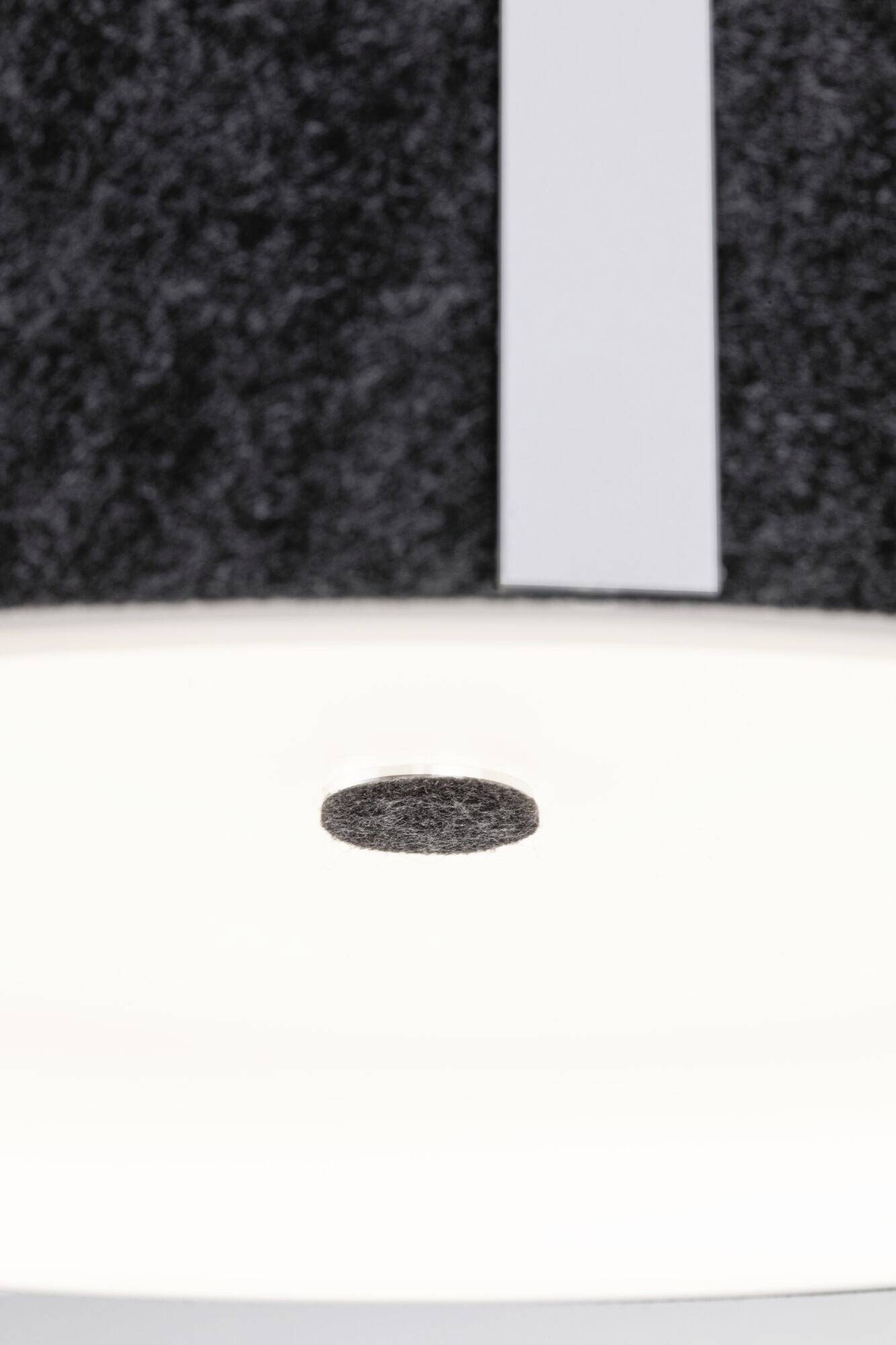Okrúhly, izolovaný plstený kotúč sa vznáša tesne nad svetlou, bielou plochou pred tmavým, štruktúrovaným pozadím.