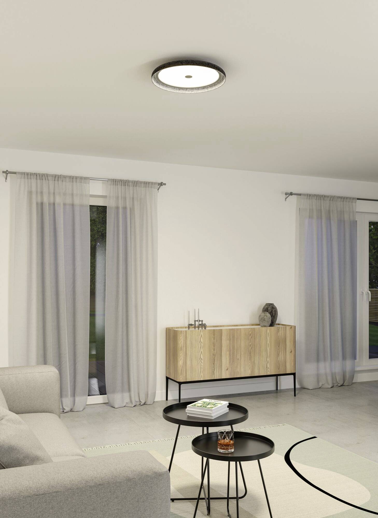 Moderná obývačka so sivou sedačkou, okrúhlymi čiernymi konferenčnými stolíkmi, drevenou komodou a jemným osvetlením zo stropnej lampy.