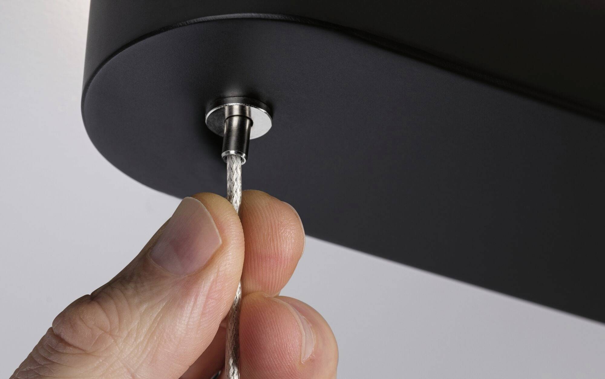 Detailný záber ruky, ktorá zasúva strieborný kábel do čierneho zariadenia.