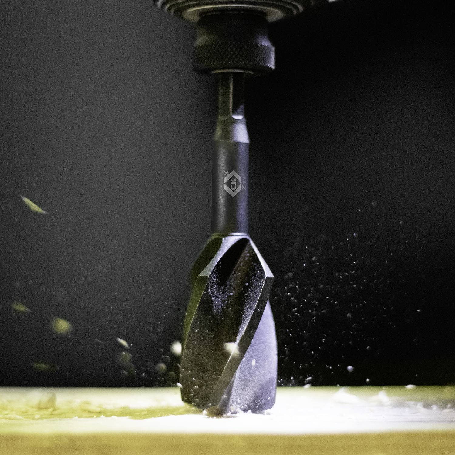 Vrták preniká drevom vysokou rýchlosťou, pričom drevené triesky lietajú do vzduchu.