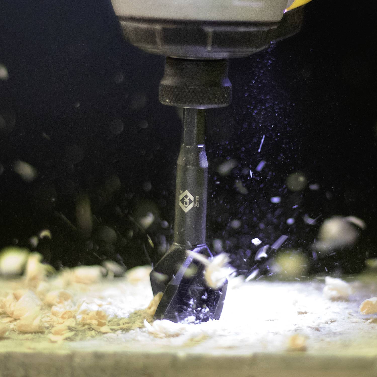 Vŕtačka pracuje na kuse dreva, pričom drevené triesky lietajú všetkými smermi. Scéna je dynamická a ukazuje silu vŕtania.