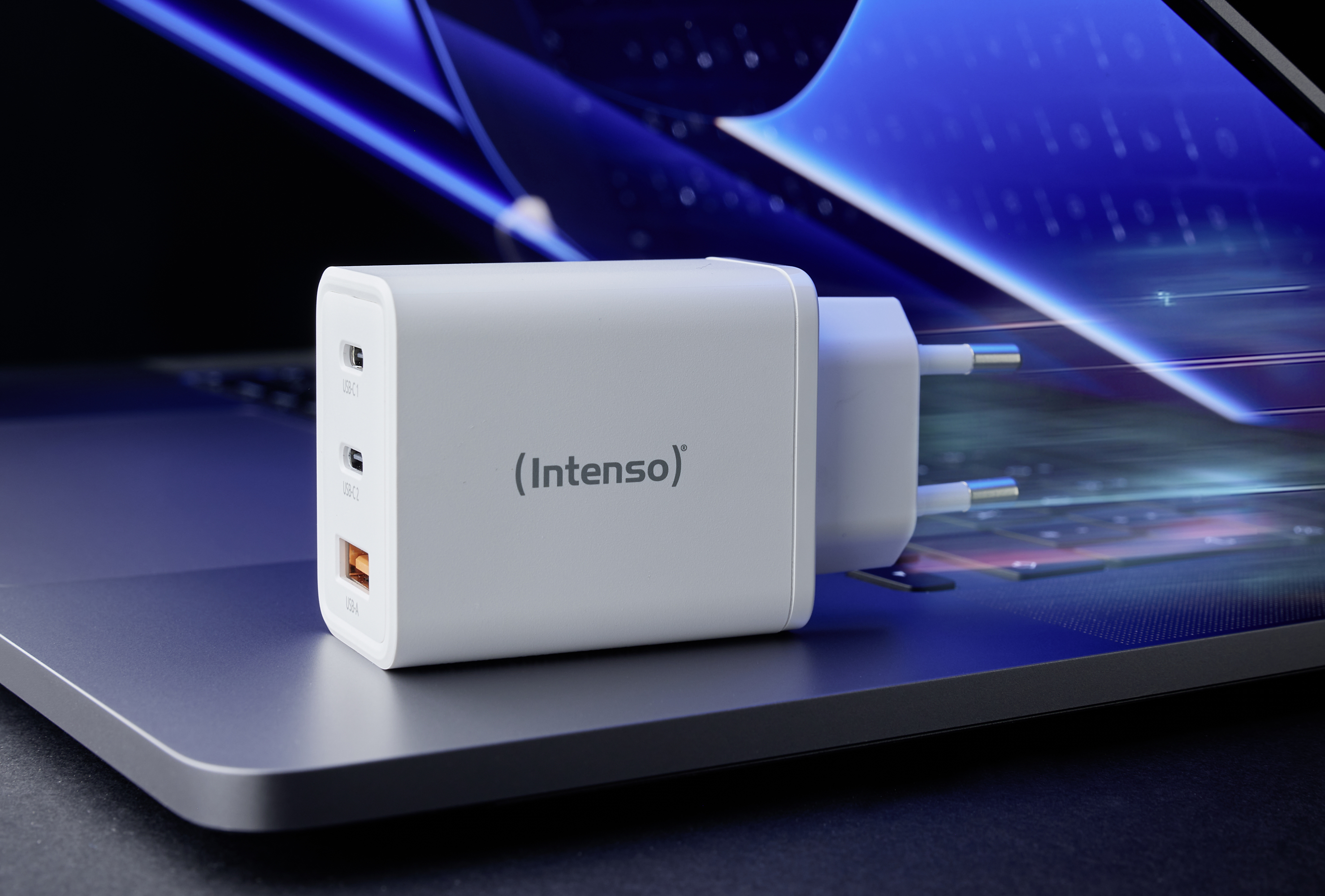 Biele nabíjačka s nápisom 'Intenso' leží na laptope. Má dva USB-C a jeden USB-A port.