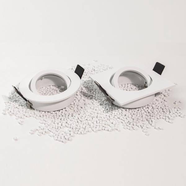 Dva biele okrúhle objekty so štvorcovými rámami ležia na bielych zrnách na hladkom povrchu.