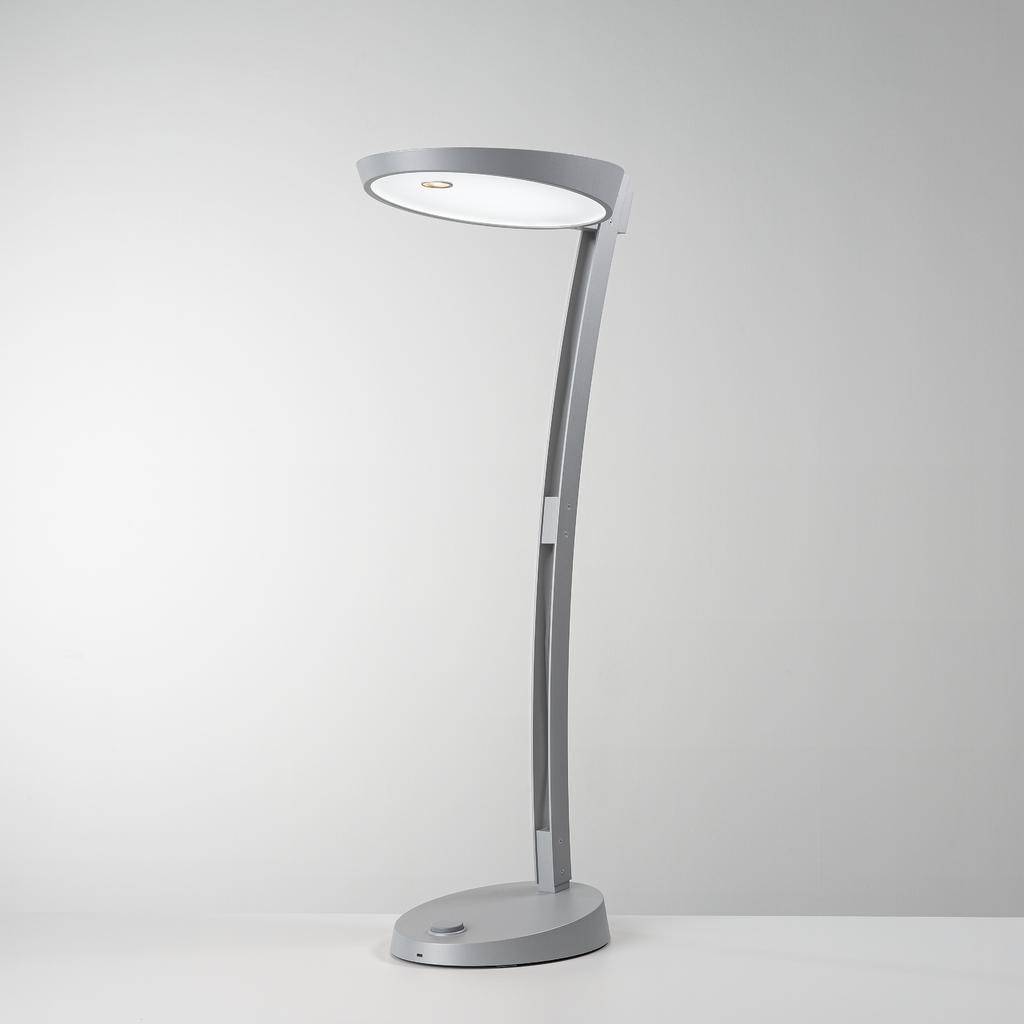 Moderná strieborná stolná lampa so zakrivený stojanom a okrúhlou, plochou svietiacou hlavou na sivom pozadí.