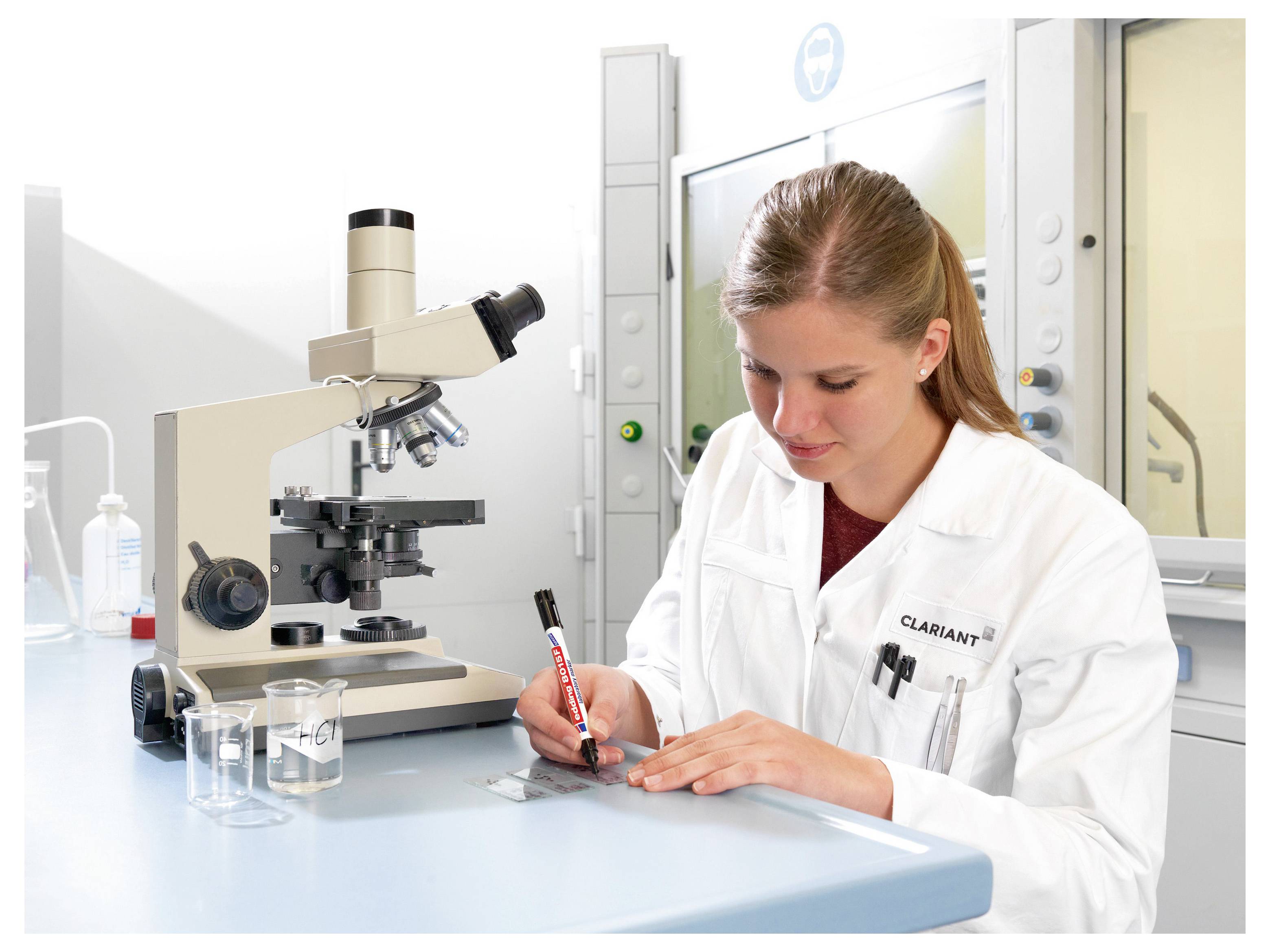 Vedkyňa v laborantskom plášti si robí poznámky vedľa mikroskopu na pracovnej stanici v laboratóriu.