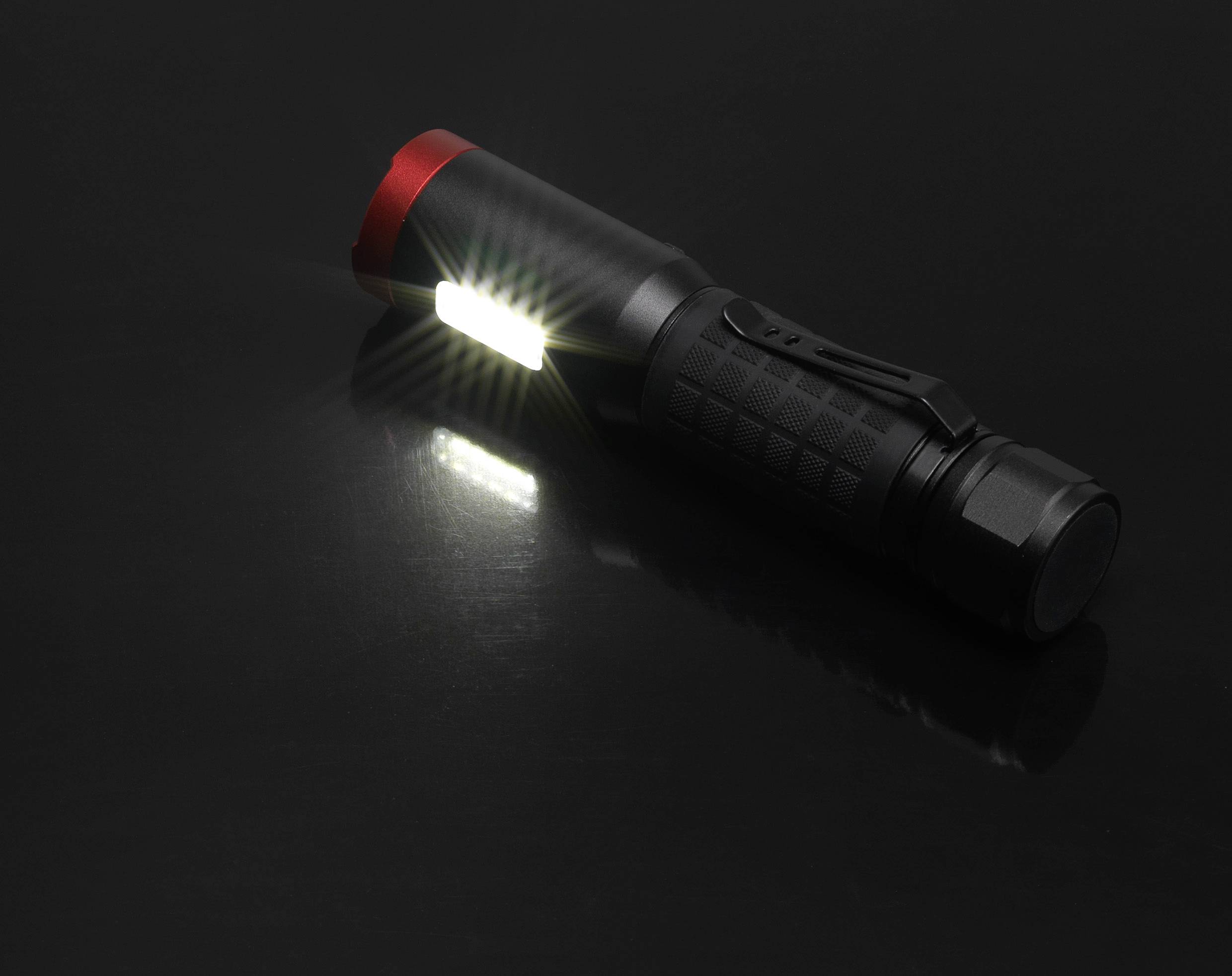 Čierna baterka leží na tmavom pozadí a vyžaruje jasné svetlo z boku.