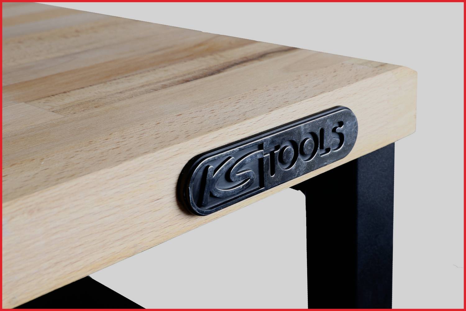 Drevená doska stola s kovovým rámom. Na hrane stola je pripevnená kovová tabuľka s nápisom 'KS TOOLS'.