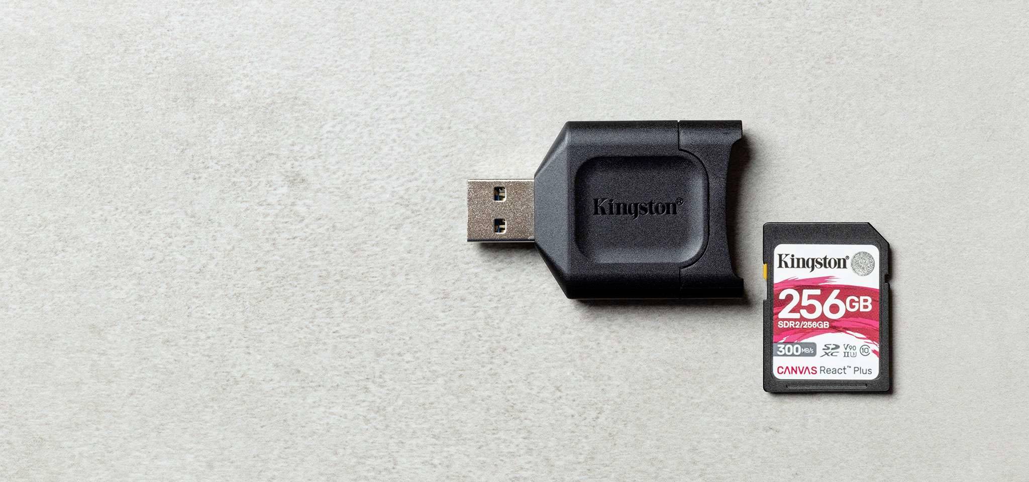 USB čítačka pamäťových kariet s 256GB SD kartou vedľa seba na sivom povrchu.