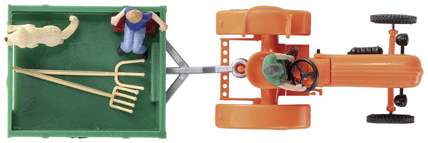 Miniatúrna figúrka na oranžovom traktoreťahá zelený príves. V prívesom sú duas vidly na seno, stojaca osoba a pes.