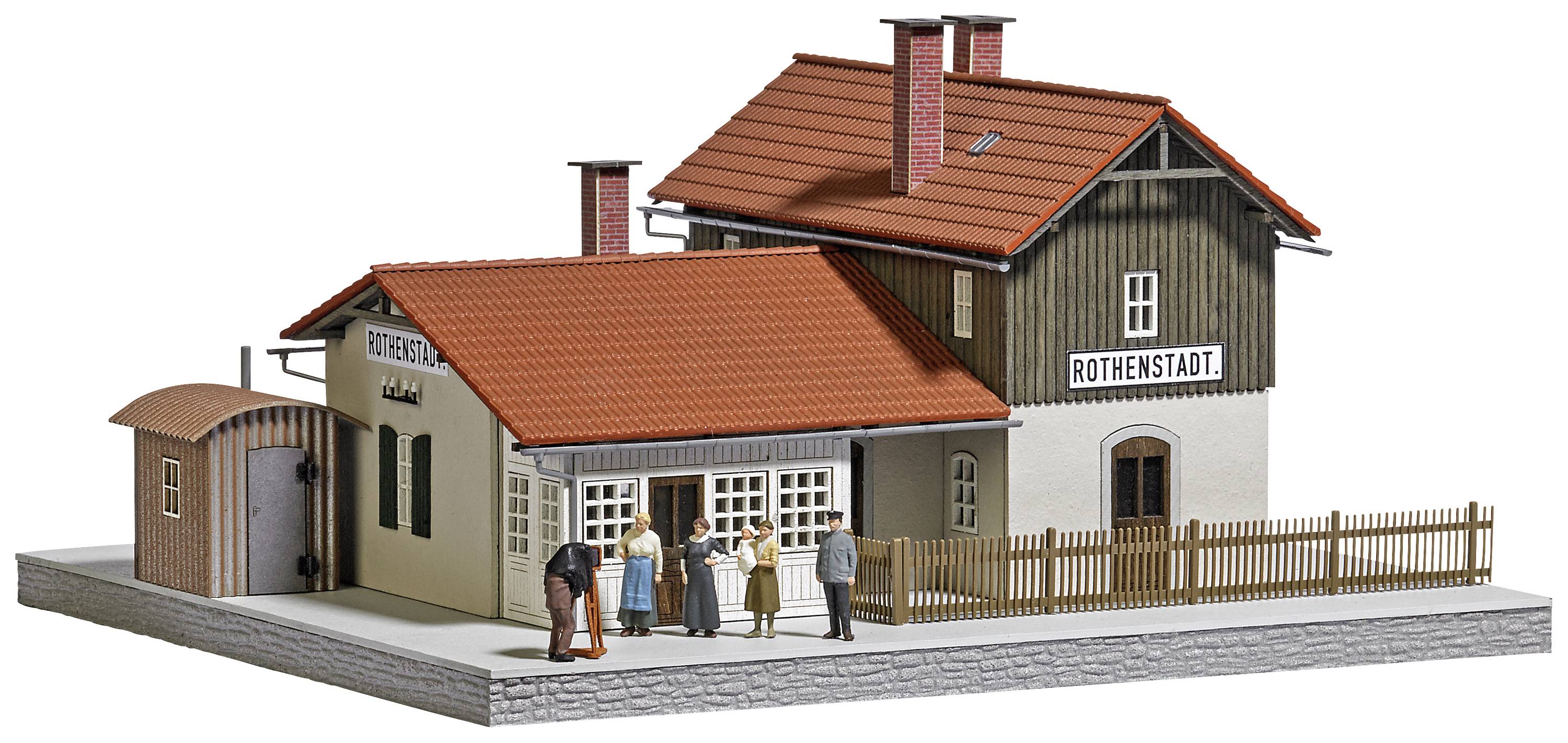 Model železničnej stanice s červenou strechou a nápisom 'Rothenstadt'. Pred budovou stoja miniatúrne figúrky vedúce rozhovor.