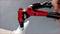 Ruka drží červené nožnice na nitovanie, ktoré zasadzujú nitku do strieborného kovového kusu. Detailný záber zachytáva proces nitovanania.