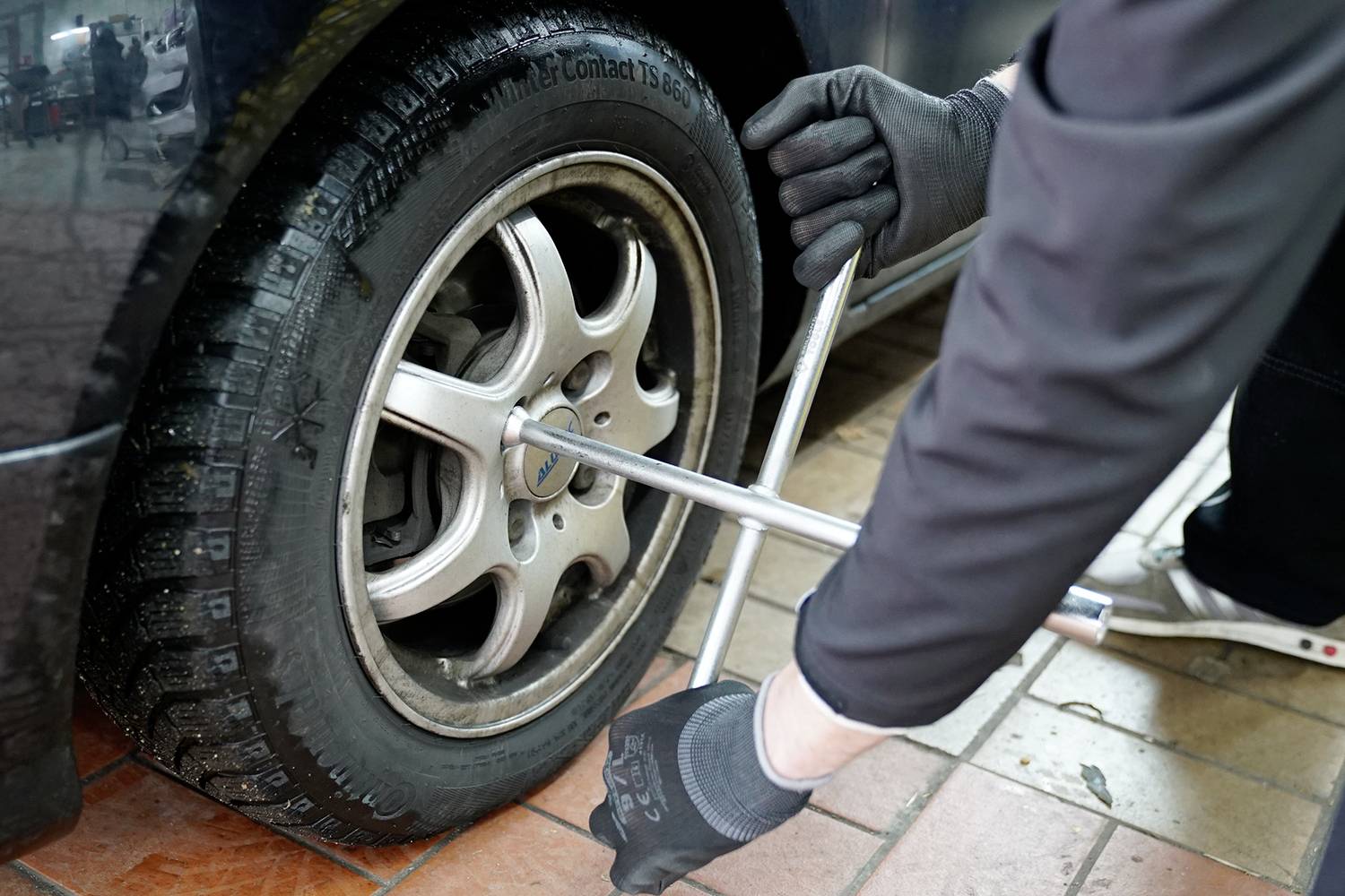 Mechanik dotiahuje maticu kolesa na pneumatike pomocou kľúča na kolesá. Pneumatika má zimný dezén.