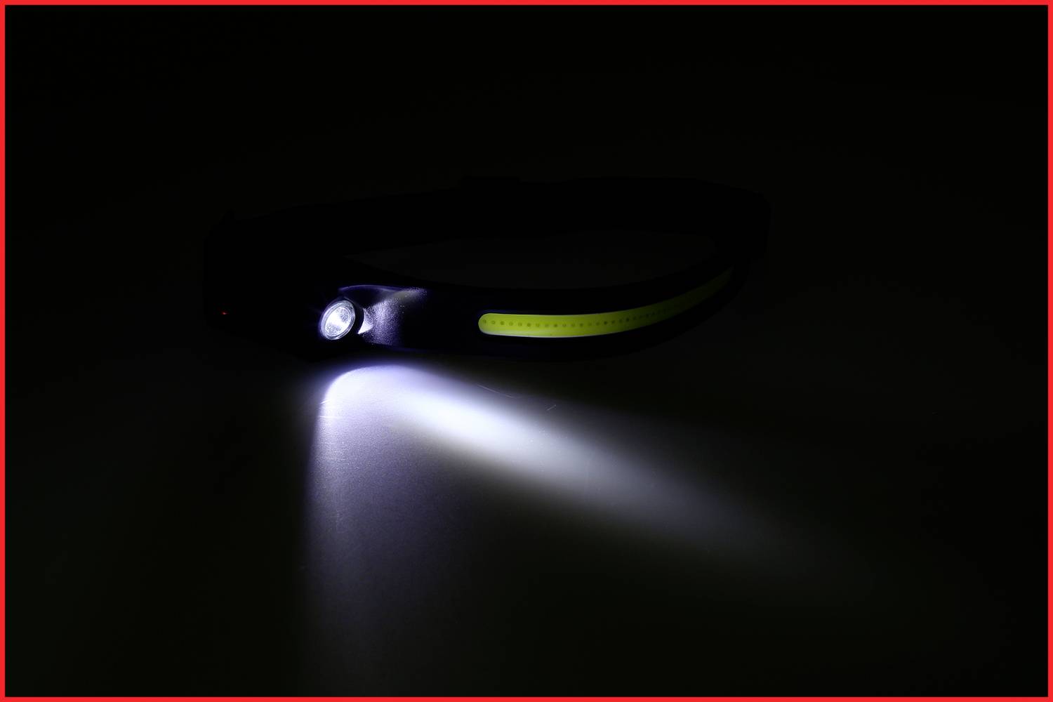 Čierna čelová lampa so zapnutým svetlom, ktoré projektuje biely lúč dopredu. Tmavé pozadie.