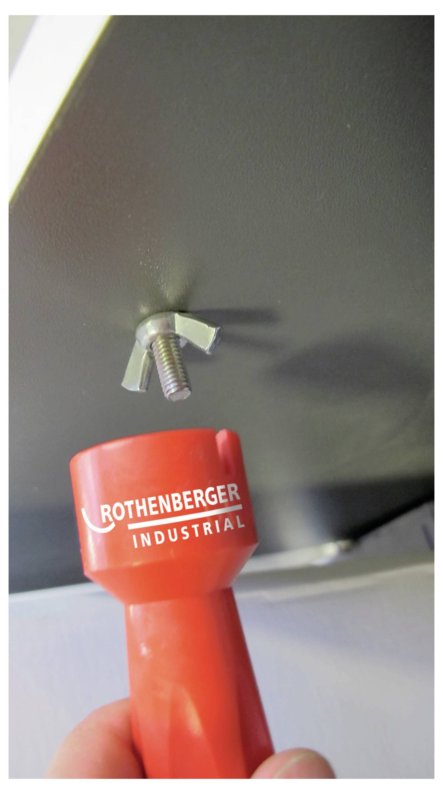 'Červený priemyselný nástroj Rothenberger sa používa na dotiahnutie krídlovej matice na skrutke.'