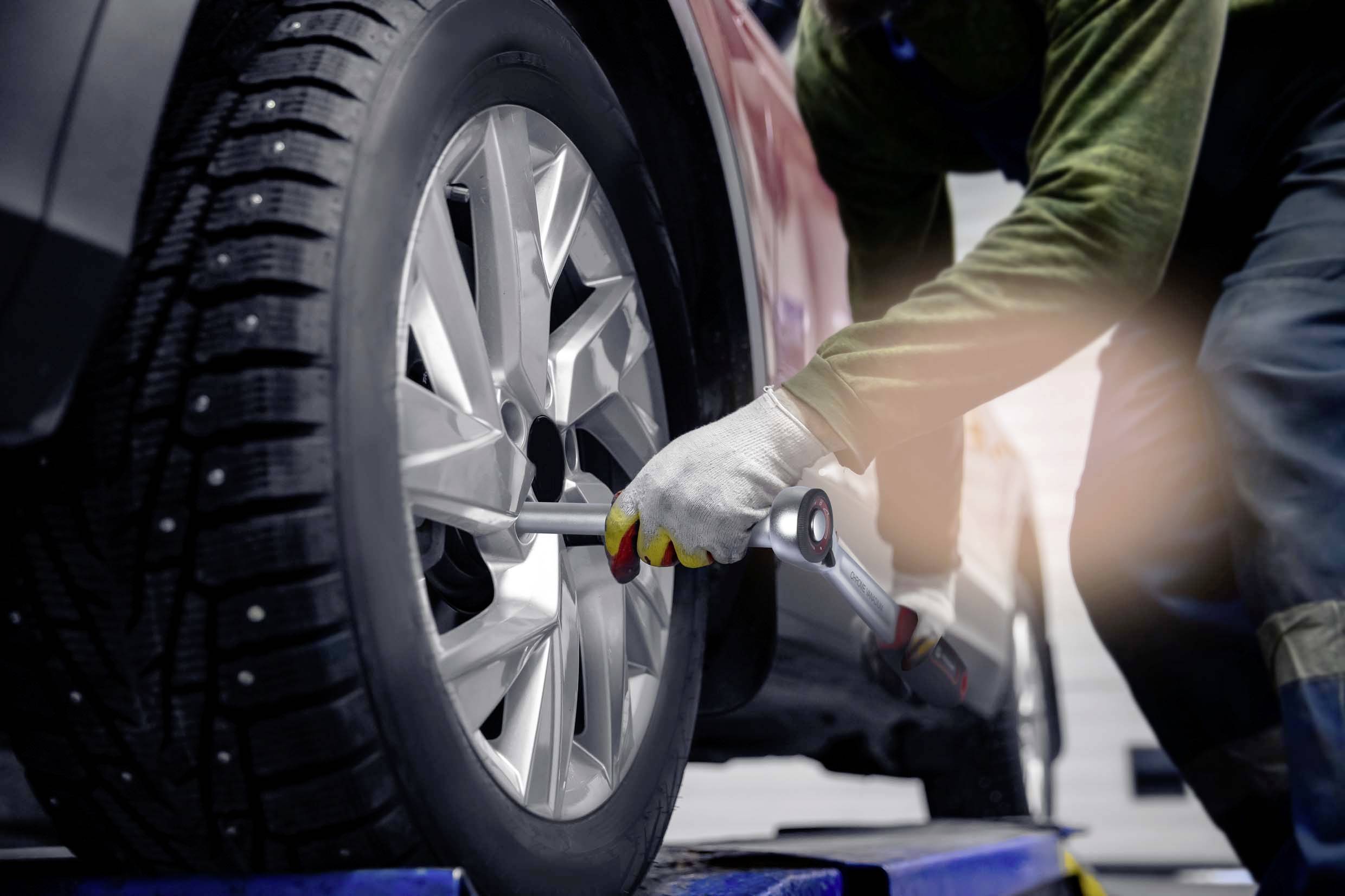 Mechanik vymieňa pneumatiku v autoservise. Auto je zdvihnuté na zdviháku a mechanik používa kľúč.