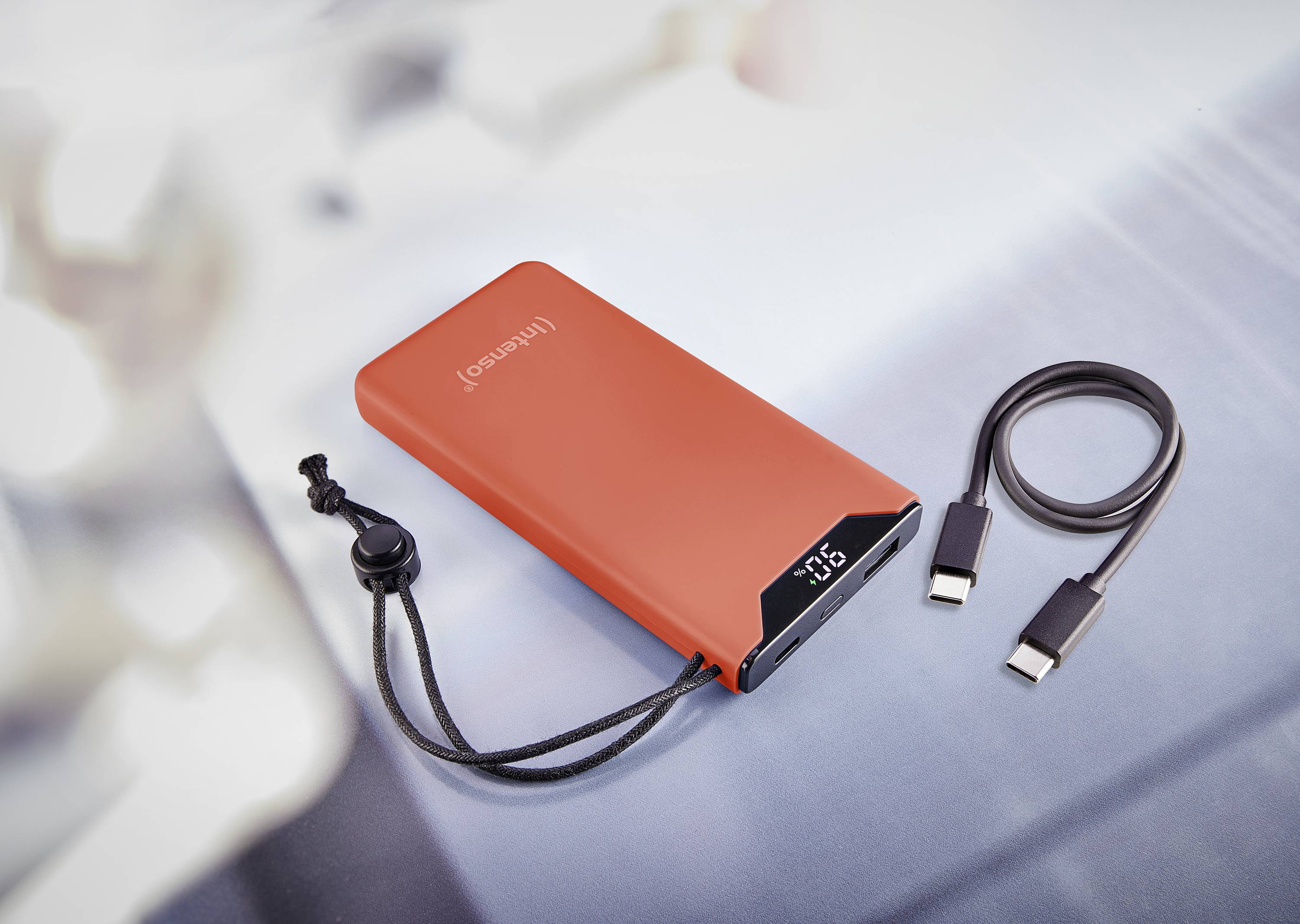 Červená powerbanka s digitálnym displejom stavu batérie. Vedľa nej leží USB kábel na rozmazanom pozadí.