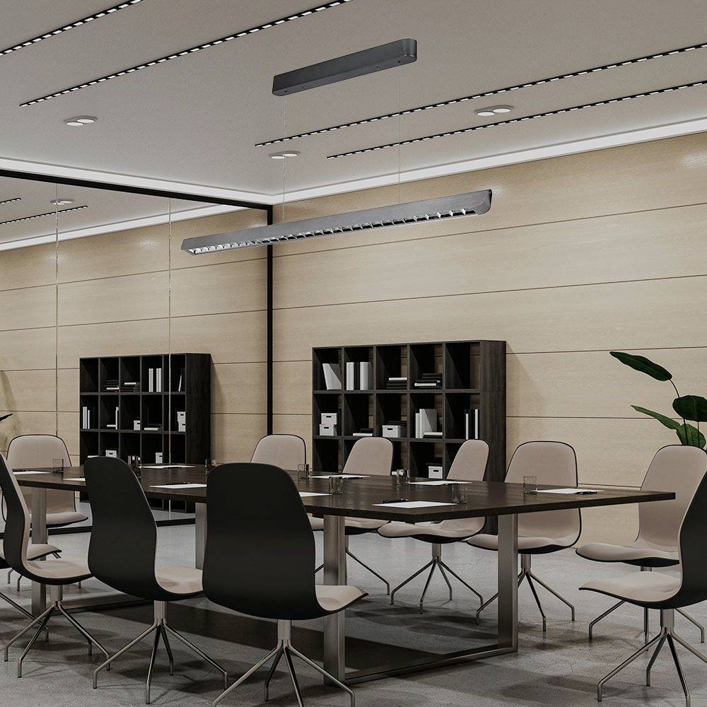 Konferenčná miestnosť s veľkým stolom a čiernymi stoličkami, police s knihami na stene, moderný osvetľovací systém, rastlina v rohu.