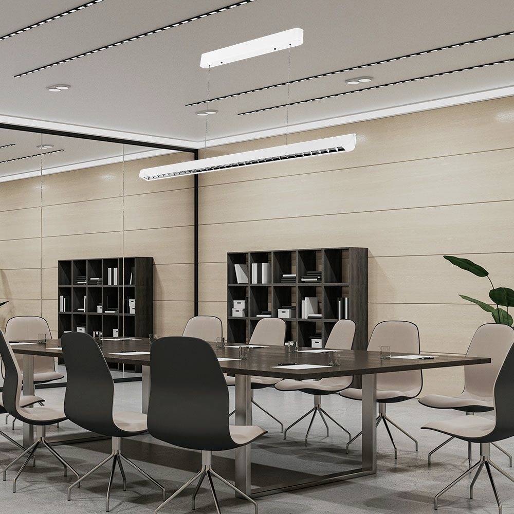 Moderná konferenčná miestnosť s veľkým stolom a stoličkami, políčkami na stene a rastlinami v rohoch. Jasné osvetlenie zo stropu.