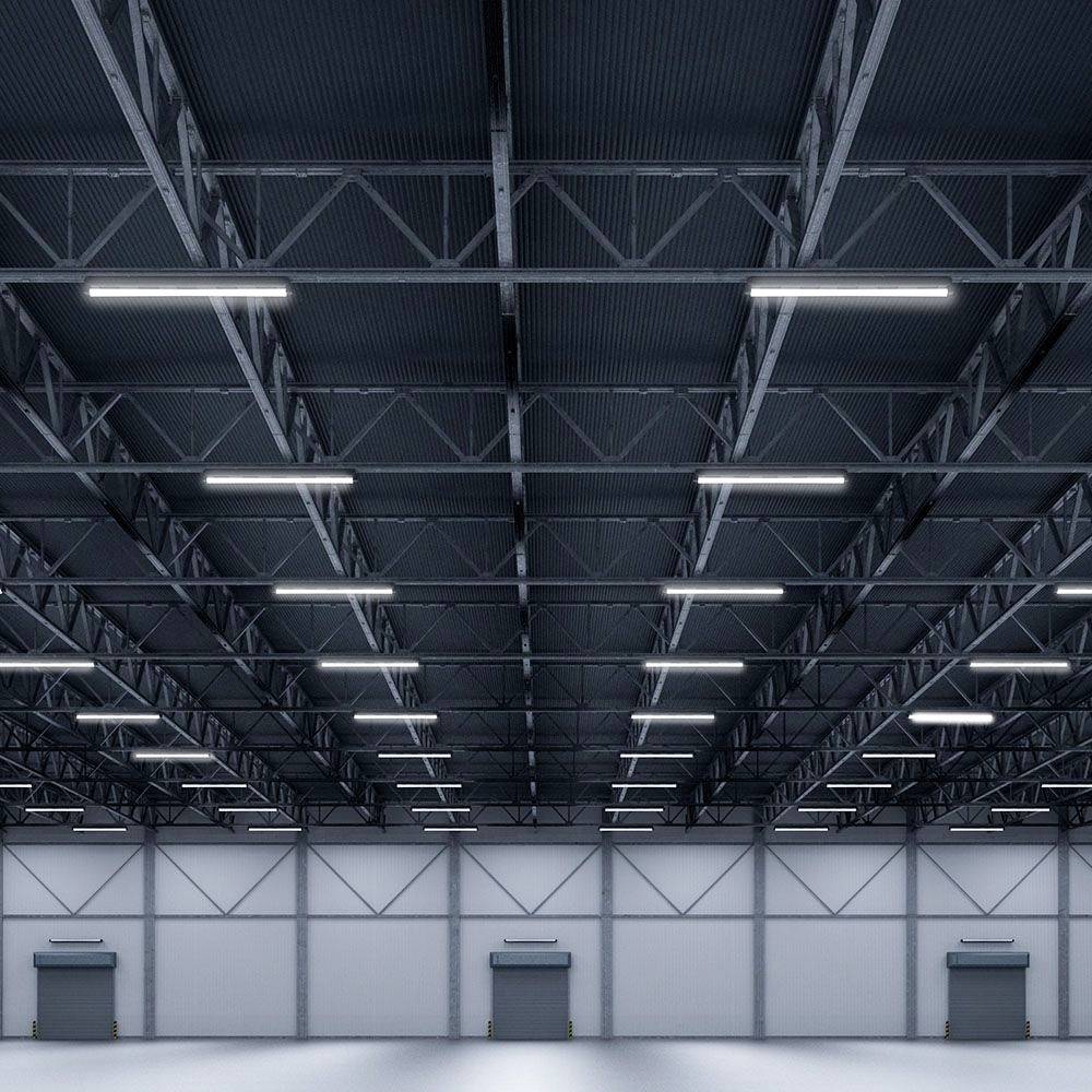 Prázdna, veľká skladová hala s vysokým stropom a oceľovými nosníkmi, osvetlená jasnými, rovnomerne rozmiestenými žiarivkami.