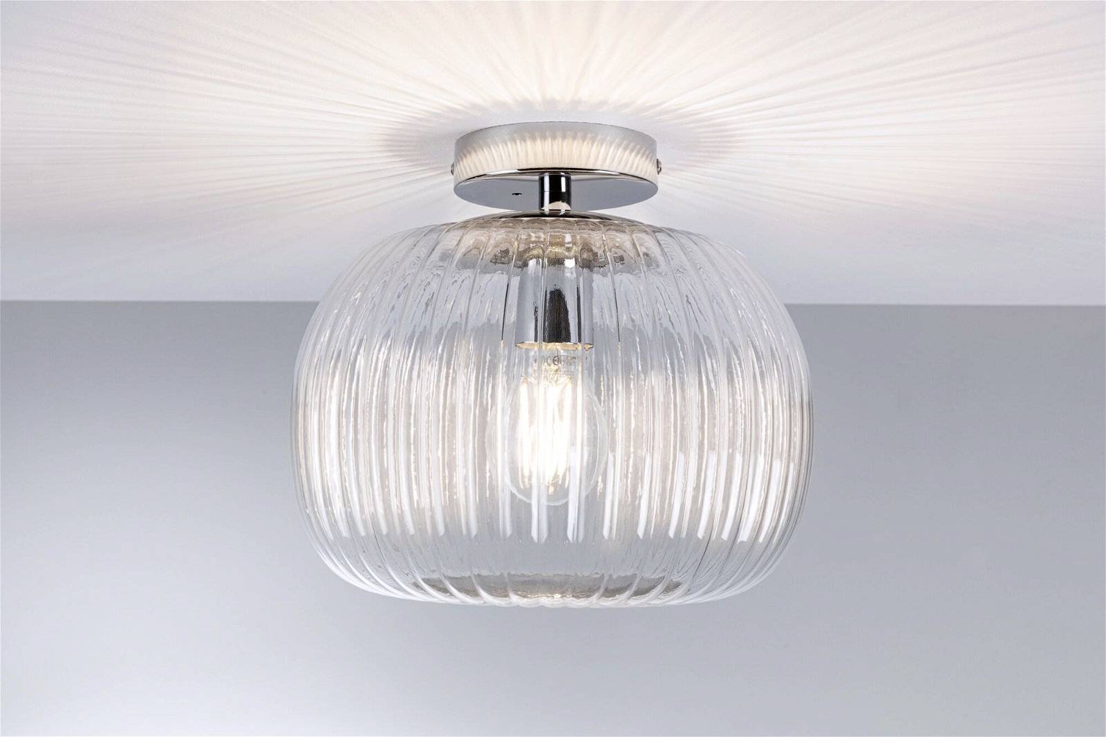 Okrúhle stropné svietidlo so štruktúrovaným skleneným tienidlom, pod ktorým je viditeľná žiarovka. Svetlo sa rovnomerne odráža na strope.