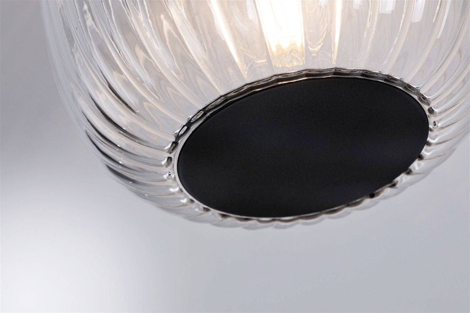 Detailný záber modernej lampy s priesvitným, vrúbkovaným sklom a čiernou kovovým podstavcom. Vyžaruje teplé svetlo.