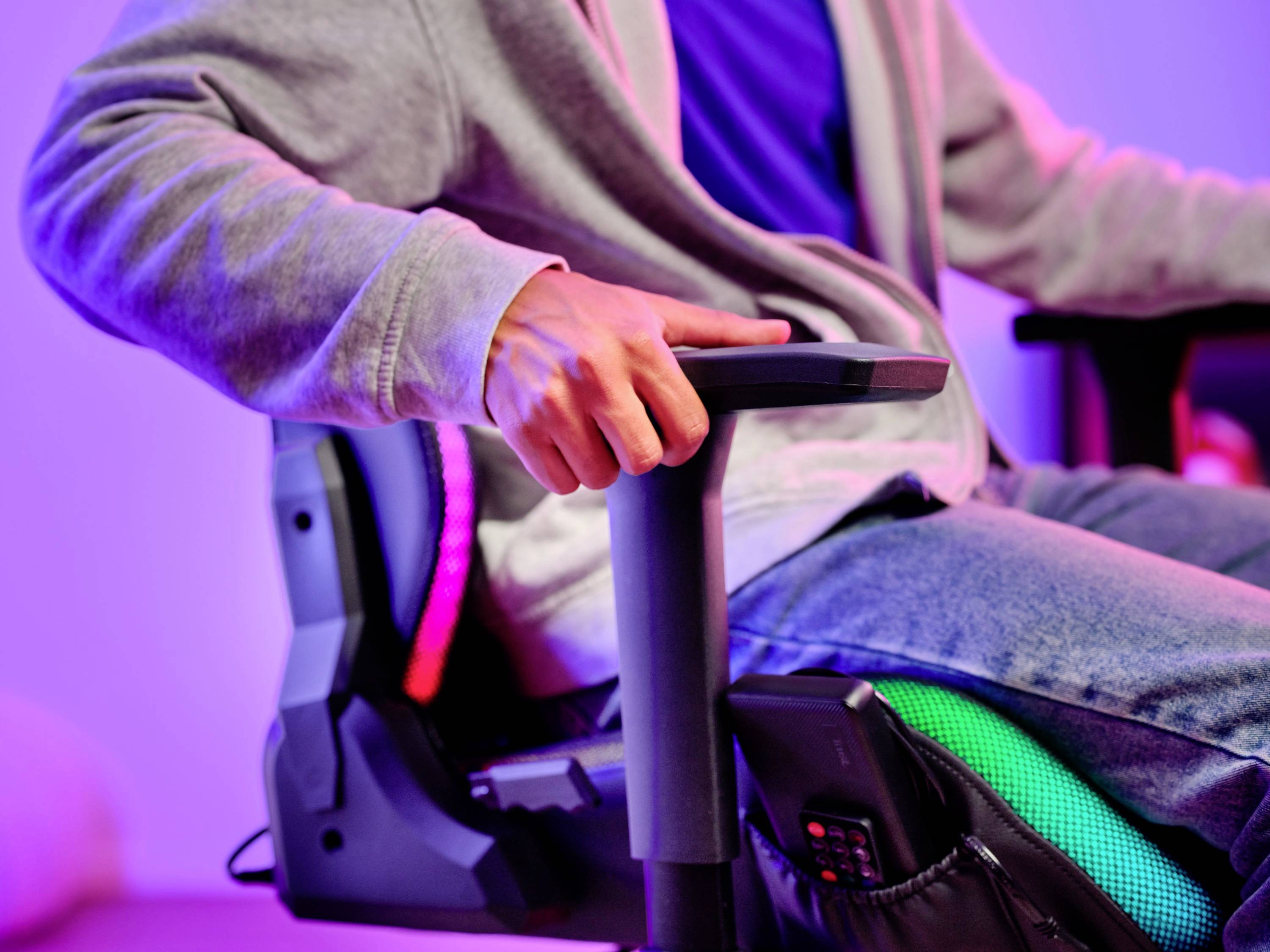 Osoba sedí v ergonomickej stoličke a drží sa opierky. Má na sebe voľnočasový odev. Dôraz je kladený na pohodlie a uvoľnenie.