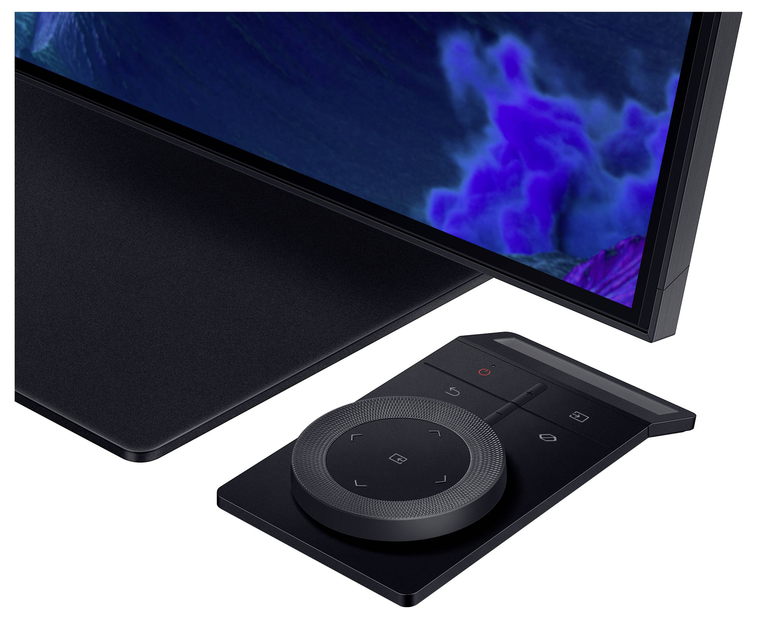 Čierny elektronický ovládač s kruhovým poľom tlačidiel leží vedľa obrazovky, ktorá zobrazuje modré a fialové odtiene.