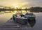 Mólo pri západe slnka s loďou vo vode. Na móle sa nachádza rybársky box a rybársky prút. Pokojná scenéria.