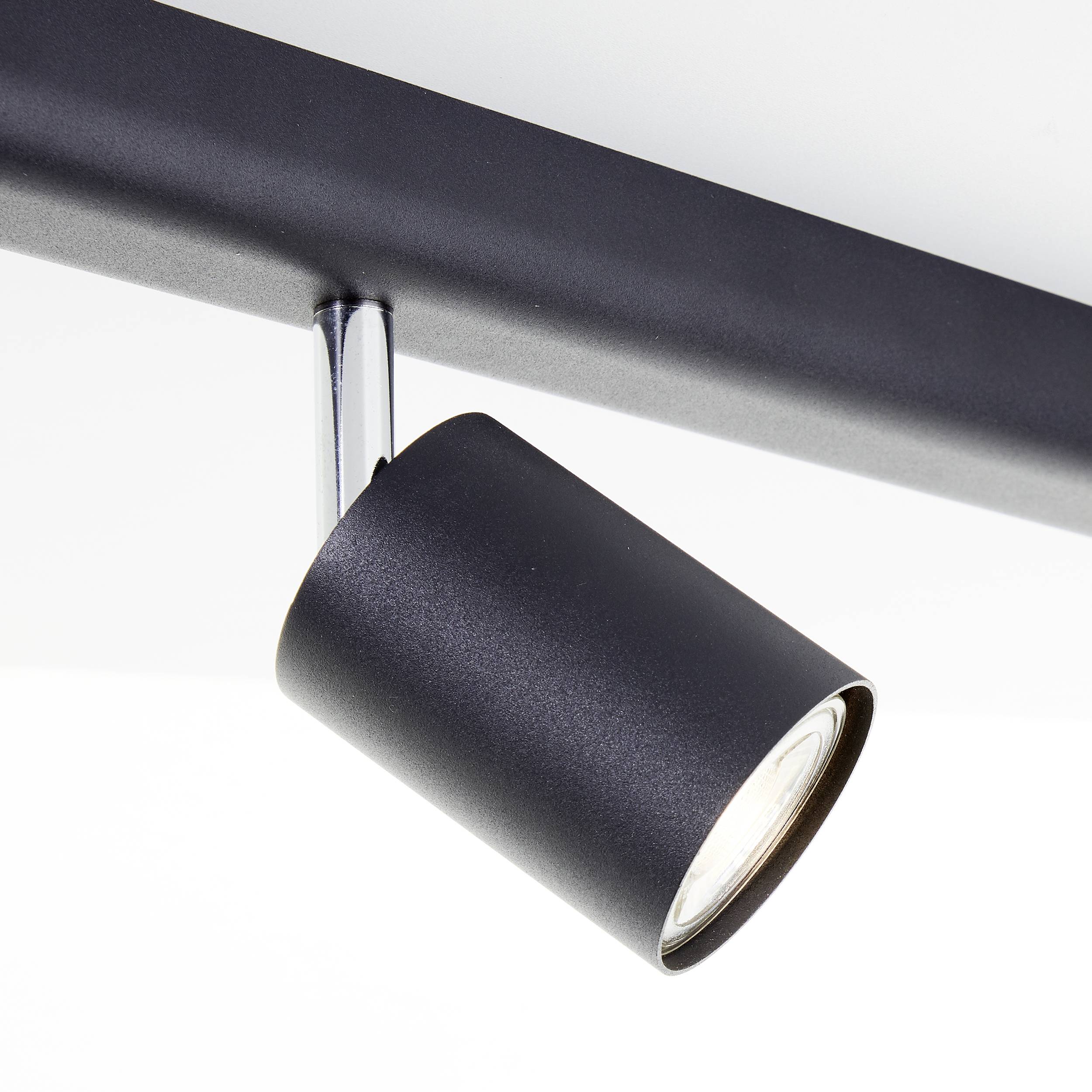 Čierny LED stropný reflektor na lište, smerujúci na svetelný bod. Moderný, minimalistický dizajn.