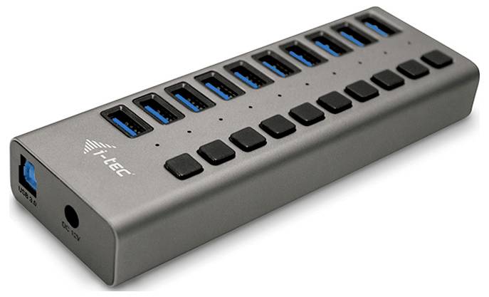 USB hub s 12 USB portami, umiestnený na obdĺžnikovom kryte. Na ľavej strane je viditeľný dodatočný vstup a značka i-TEC.