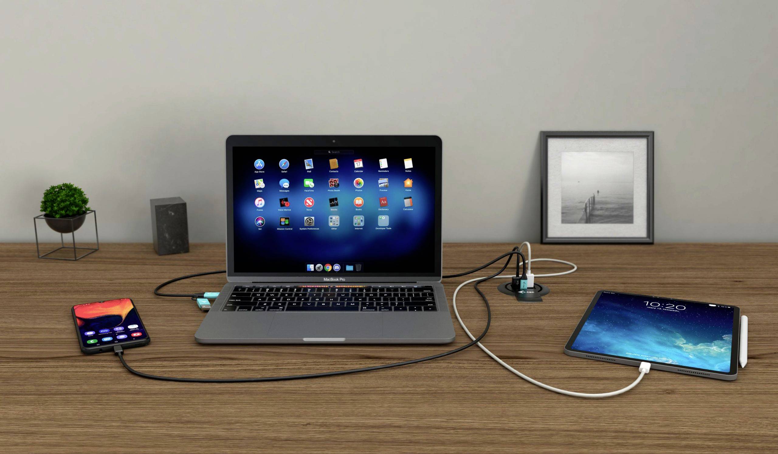Laptop, tablet a smartfón sú na stole navzájom prepojené za účelom synchronizácie dát. V pozadí visí zarámovaný obraz.