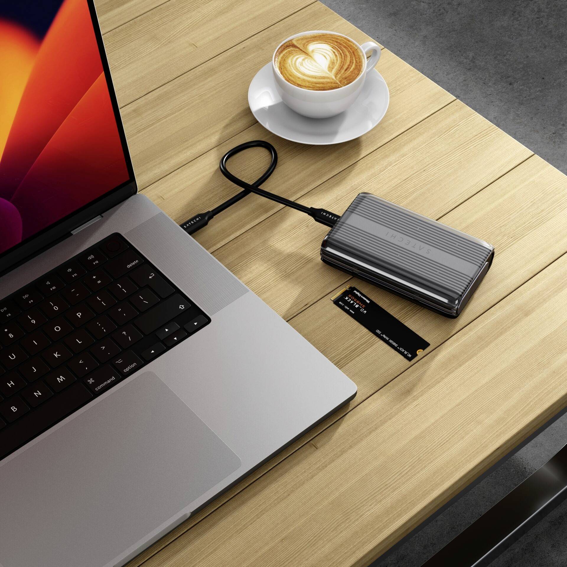 Laptop s externým harddiskom, kreditnou kartou a cappuccinom na drevenom stole.