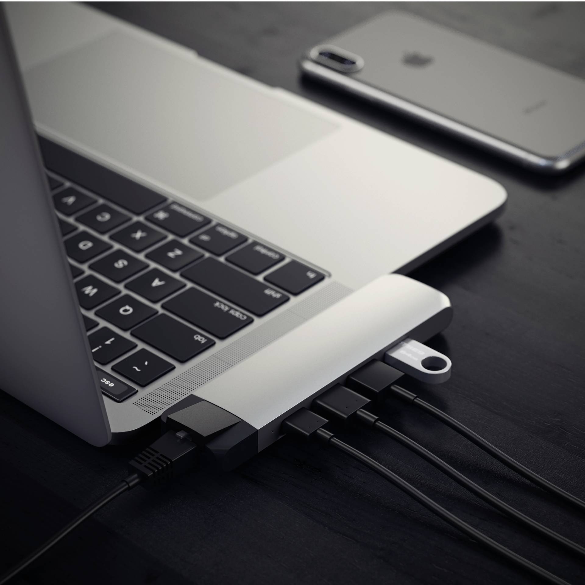 Laptop s pripojeným USB rozbočovačom; niekoľko káblov a USB kľúč sú pripojené. V pozadí leží smartfón.