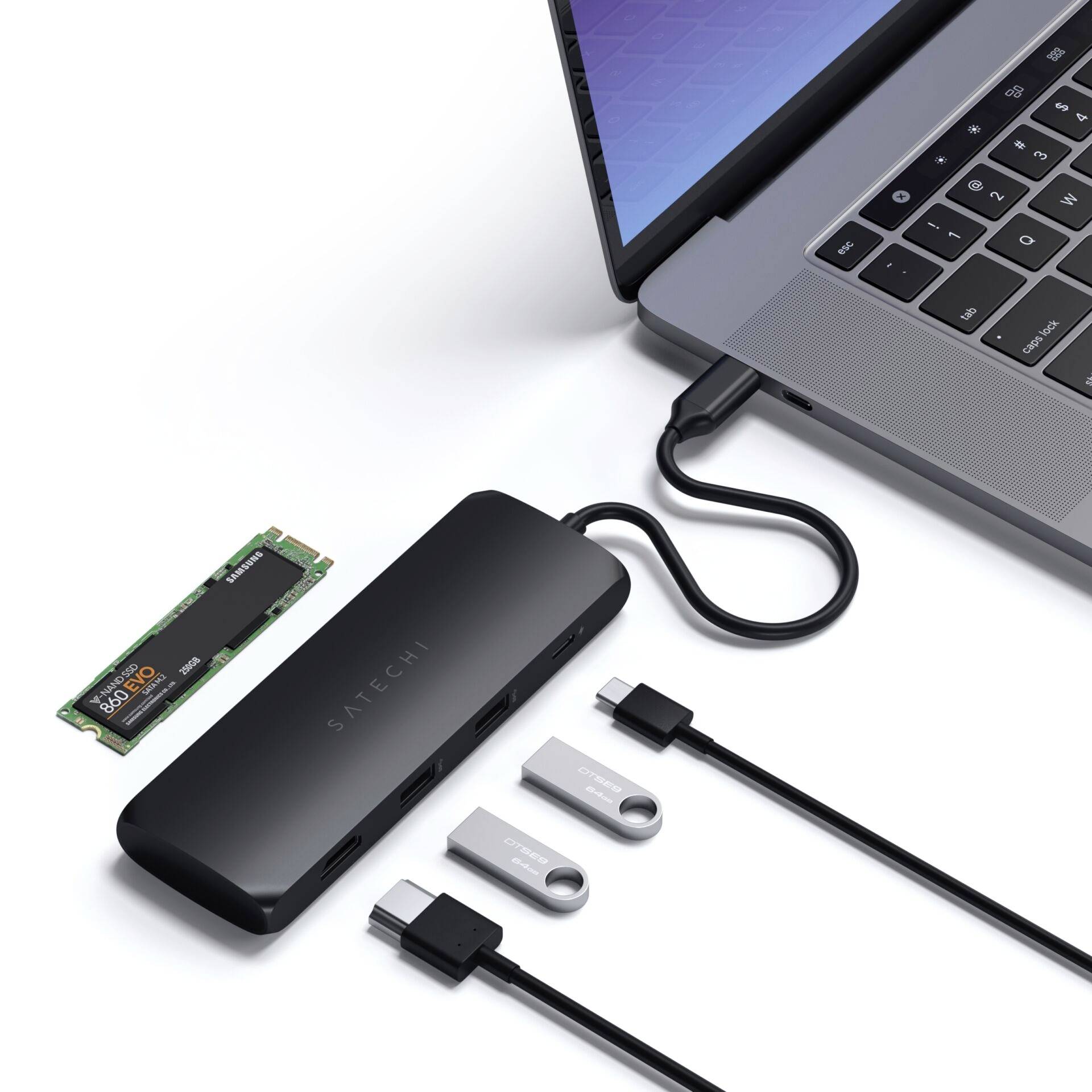 Laptop s otvorenou obrazovkou je pripojený prostredníctvom dvoch USB kľúčov a čiernej dokovacej stanice. Vedľa leží modul M.2 SSD.
