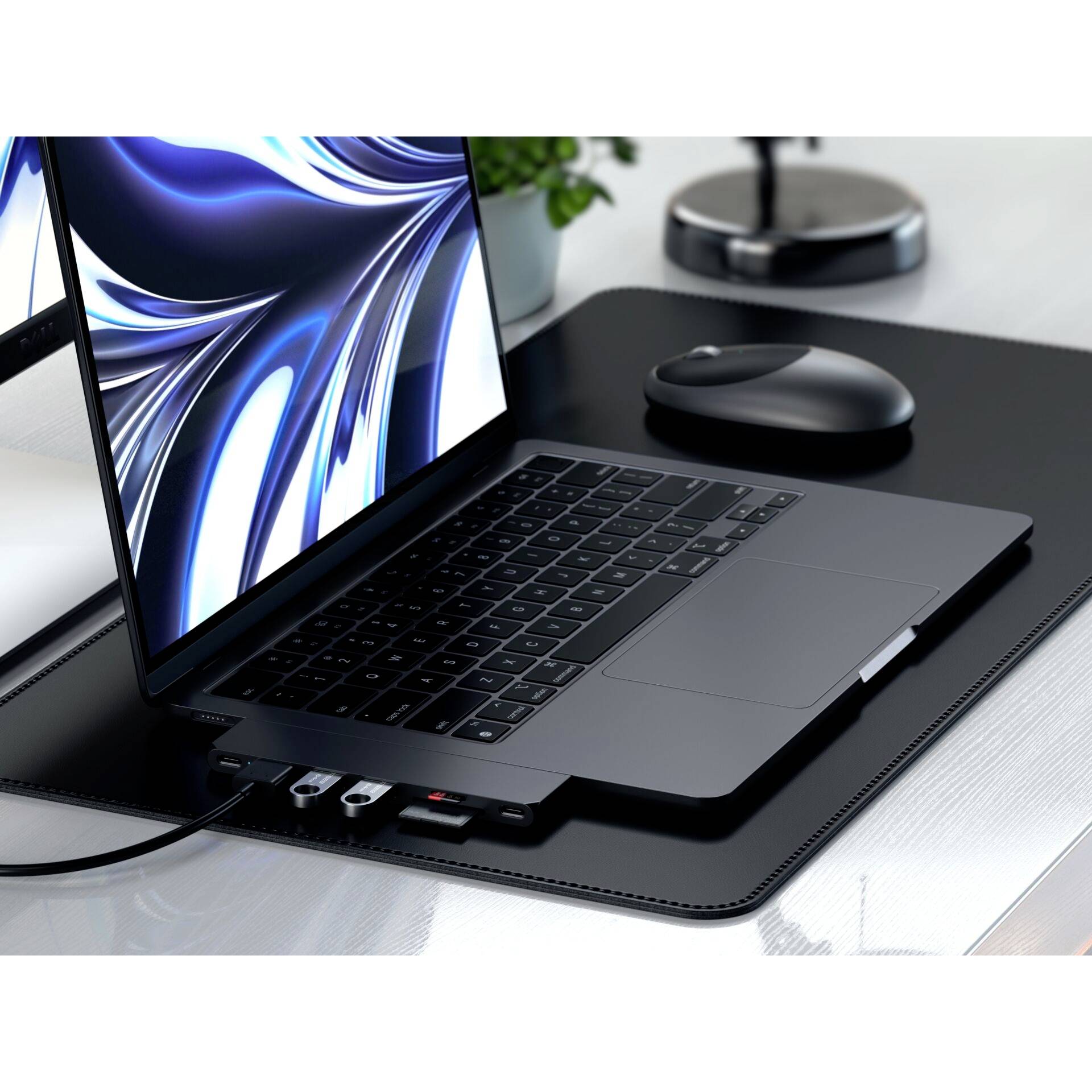 Otvorený laptop na stole, s pripojeným USB hubom a myšou vedľa neho. V pozadí je rastlina.