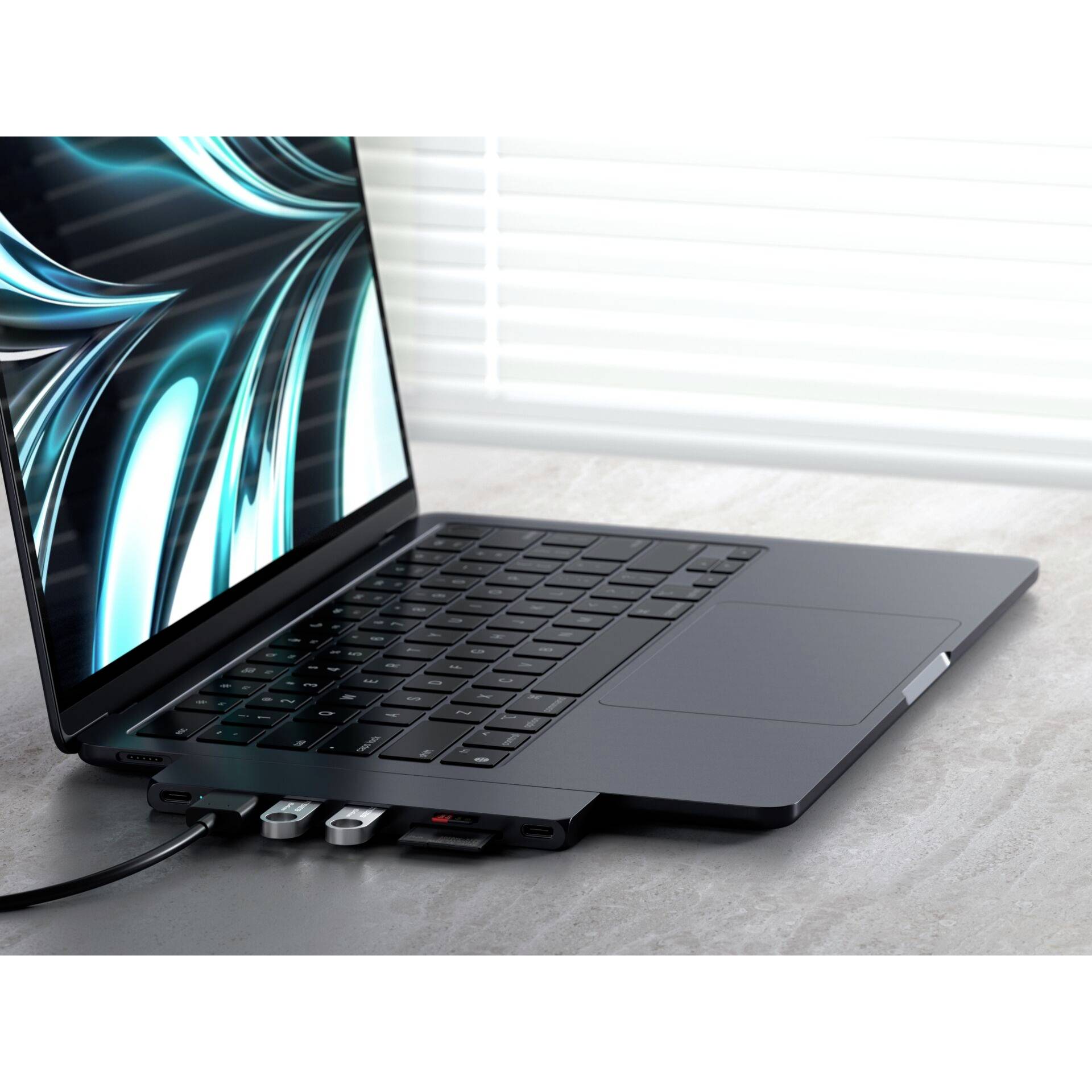 Laptop na stole, ku ktorému sú pripojené viaceré USB kľúče a jeden kábel. Na obrazovke je viditeľný abstraktný vzor.