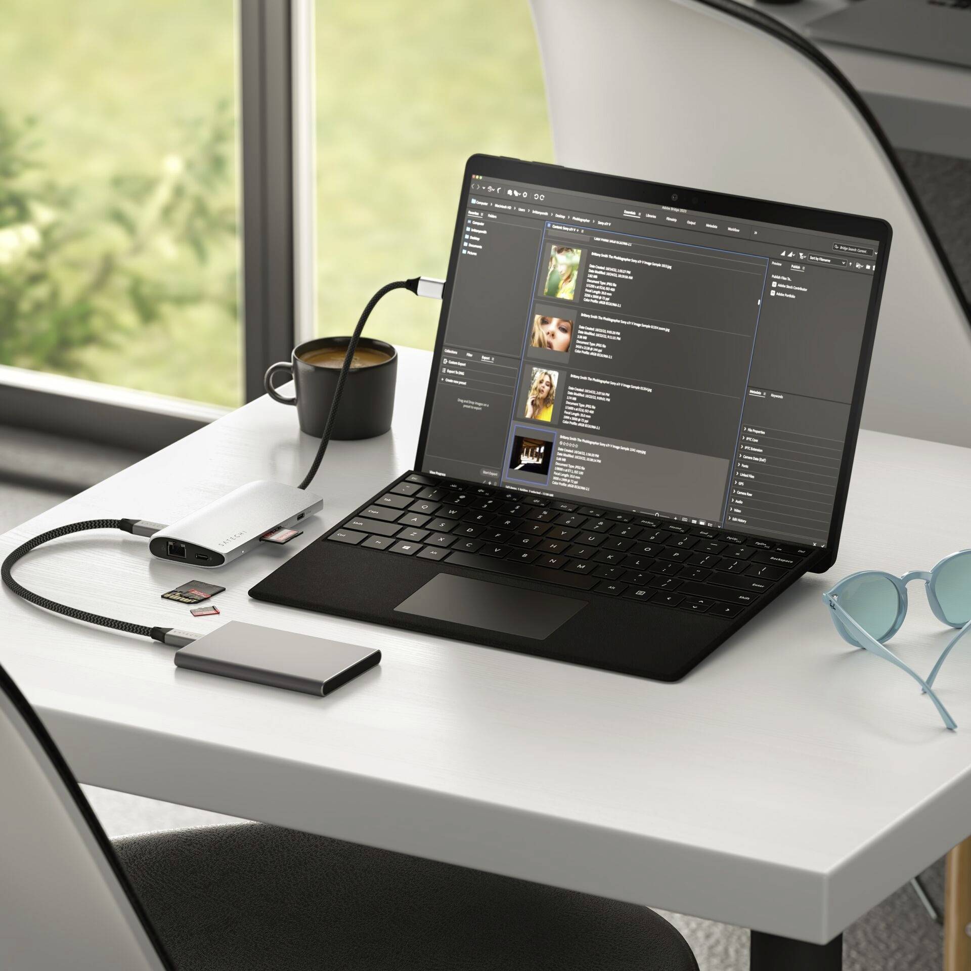 Na stole leží notebook, na ktorom je otvorený hudobný program. Vedľa notebooku stoja šálka, externý disk, USB hub a slnečné okuliare.